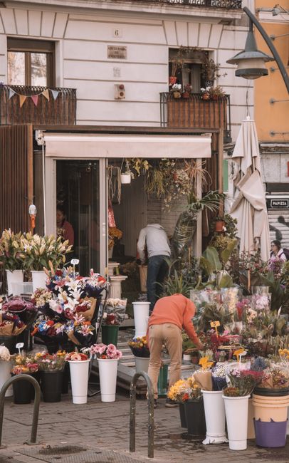 A bustling flower shop on Maidenhead High Street, showcasing an array of fresh flowers in vibrant colours arranged in various vases and containers outside the store, with some flowers spilling into wh