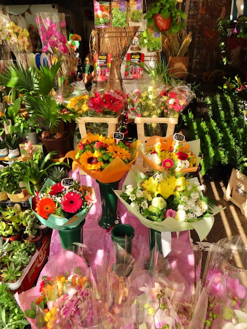 A variety of fresh flower bouquets are displayed on tables at a flower shop, including a vibrant arrangement of yellow and orange flowers wrapped in yellow paper, pink and white blossoms in white and 