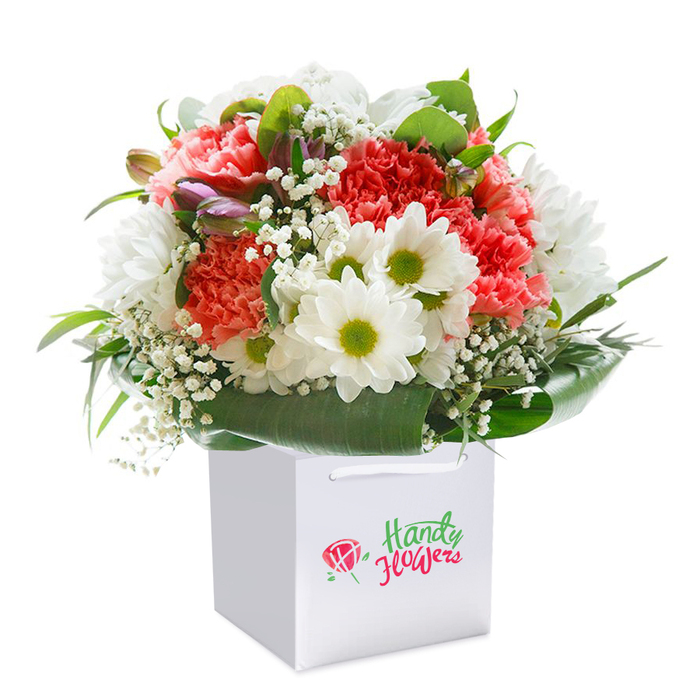 Set against a spotless white backdrop, a vibrant and artistically arranged floral bouquet stands tall in a snow-white gift bag-its structured, modern lines offset by the organic abundance within. Highlighted by clusters of soft coral-beige carnations, identifiable by their generously ruffled edges, the arrangement is interspersed with crisp, daisy-like white chrysanthemums whose bright lime centers add a playful touch. Wisps of cloudlike baby's breath are woven among the larger flowers, lending a lightness and intricate texture, while deep emerald leaves and broad foliage anchor the design. Brief glimpses of purple-tinged buds, possibly alstroemeria yet to open, peek from the bouquet's left side, bringing an element of unfolding promise. The whole display radiates freshness and classic sophistication, reminiscent of Maidenhead's riverside gardens and the serene elegance found strolling through the town's historic heart. Completed by a sturdy white ribbon handle on the smart gift bag, this bouquet exudes both style and convenience-perfect for delivery to loved ones whether celebrating a birthday, anniversary, or simply sharing an act of kindness. Each flower is expertly placed, the rounded shape and lush greenery a signature of quality local floristry. Branded modestly, the arrangement is photographed under clear, even light, which amplifies the intense corals, crisp whites, and verdant greens to convey both the visual brilliance and emotional impact of a truly thoughtful gift, expertly crafted for someone special in Maidenhead.