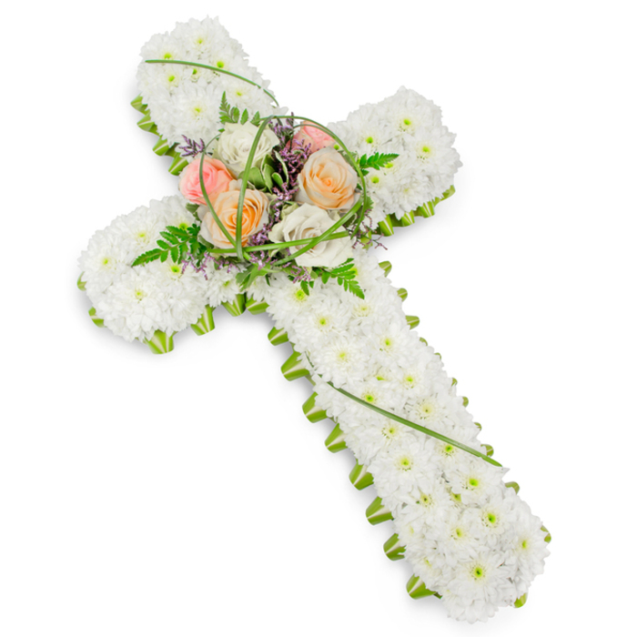 A dignified floral cross dominates the image, carefully crafted for a funeral or memorial tribute and shown against a simple white background that allows every detail to stand out. The entire surface of the cross, from the top arm to the base, is tightly carpeted with immaculate white chrysanthemums or similar small white blooms. Each flower is placed so closely to its neighbour that the effect is almost like finely textured fabric, soft to the eye and full of gentle depth. Around the perimeter of the cross, a narrow but striking edging of crisp green foliage defines the outline, tracing the arms and the base with a neat, living border. This combination of white and green feels both traditional and fresh, echoing the calm greenery of Maidenhead's riverside paths and nearby parks. At the central intersection, a carefully composed cluster of feature flowers rises delicately above the base layer. Here, roses in soft peach, pale blush pink, and creamy ivory create a warm focal point, their open cups and spiralling petals full of tenderness and grace. They are surrounded by lacy fern fronds, slim arcs of bright green grass, and a fine scattering of tiny purple filler flowers, which blend harmoniously while adding subtle variation in texture and colour. The cross is gently angled, giving a sense of three-dimensionality and suggesting how it might appear resting near a coffin or displayed on an easel at a church service in Maidenhead. Overall, the arrangement communicates respect, solace, and the comforting symbolism of faith, making it an appropriate choice for honouring a loved one's life and offering support to grieving family and friends.