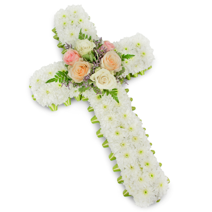 A traditional floral cross designed as a sympathy tribute is captured against a bright white studio background, the clarity of the setting drawing full attention to the workmanship. The cross is formed with broad, padded arms, every visible surface completely covered in a tight mosaic of small white chrysanthemum button flowers. Each petite bloom overlaps the next, creating a thick, cushion-like texture that feels calm and reassuring to the eye, symbolising purity and the gentle release of grief. Along the entire perimeter of the cross runs a finely applied lime green ribbon, which acts like a frame; it emerges just beneath the petals in an even line, adding definition to the shape and a subtle touch of fresh colour. At the intersection where the horizontal and vertical beams meet, a cluster of premium roses becomes the emotional centrepiece. These roses are fully open, their petals spiralling in layers of soft colour: delicate pastel pinks, muted peach or apricot tones, and soothing creamy whites. They are tucked among soft green fern fronds and tiny sprigs of lavender or light purple filler blooms, which introduce graceful movement and gentle contrast. The floral cross feels appropriate for a funeral or memorial in Maidenhead, perhaps placed near the front of a chapel or beside a photograph at a wake in one of the town's community venues. The composition reflects the steady hand of an experienced florist, offering a visual expression of sympathy, remembrance, and quiet faith for families saying goodbye.