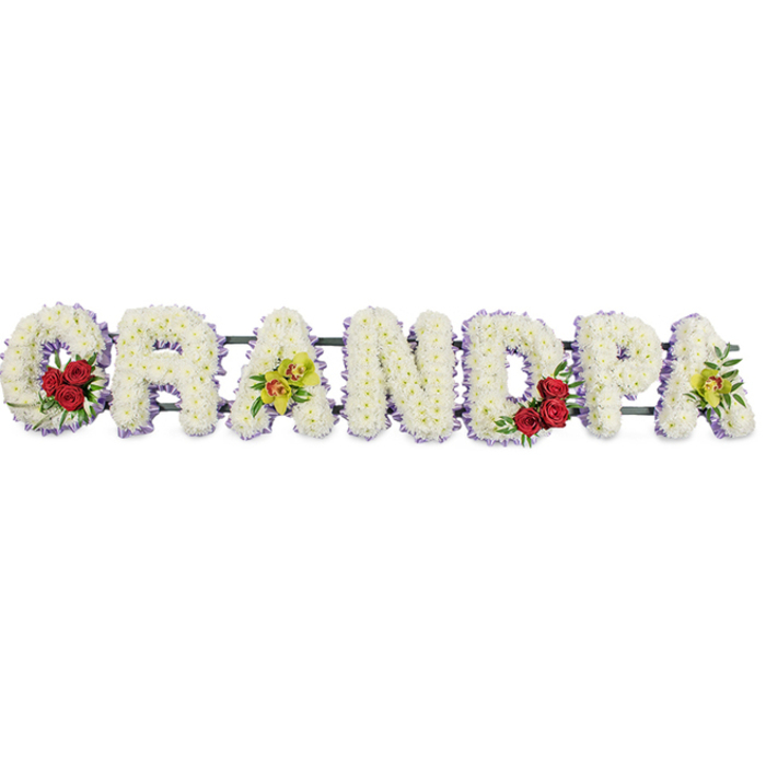 A lovingly designed funeral tribute spells out the word GRANDPA in large, upright capital letters, arranged in a single horizontal row against a bright white background that keeps all attention on the flowers. Each letter is formed from masses of closely placed white chrysanthemums, their small, rounded petals creating a thick, plush surface that looks soft to the touch, like a comforting pillow. Tracing the edges of every letter, a neat border of pale purple ribbon or trim adds just enough contrast to define the shapes clearly, much as soft morning light defines the rooftops and treetops around Maidenhead's quiet residential streets. At the start of the tribute, the curve of the G is enriched with a vivid cluster of three or four deep red roses, surrounded by sprigs of dark green foliage that stand out boldly against the white blooms. The third letter, A, is gently embellished with yellow-green orchid blossoms, some with delicate reddish markings in their throats, lending an elegant, slightly exotic note. In the rounded space of the D, another grouping of red roses mirrors the first, symbolising repeated memories of love, while the final A carries a second touch of those bright orchids, visually tying the tribute together. The letters are fixed to a discreet supporting frame with narrow connecting bars, ensuring they align perfectly to form a strong, readable word for mourners gathering at local Maidenhead chapels or gravesides. Together, the cool white flowers convey serenity and honour, the roses speak of deep, enduring love, and the orchids add a sense of refinement and lasting remembrance for a treasured grandfather.