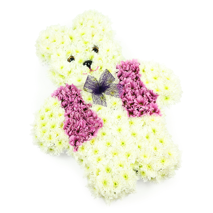 A tender teddy bear-shaped floral arrangement is captured in this image, carefully designed as a tribute for funerals, children's services, or moments of heartfelt remembrance. The bear itself is fully sculpted from clusters of white and very pale cream chrysanthemums, arranged so closely together that they form a soft, rounded surface across the head, tummy, arms, and paws. Each tiny bloom contributes to a plush, toy-like effect, reminiscent of a beloved teddy held close on quiet evenings. The facial details are simple yet expressive: two dark, bead-like eyes sit symmetrically above a small black nose, while a whisper of pink around the muzzle line suggests a faint, comforting smile that feels both gentle and protective. Across the chest, the design transforms into a floral waistcoat, created from richer pinks and mauves that add depth and warmth to the otherwise snowy palette. These coloured flowers are shaped into panels that mimic lapels, adding a touch of character and making the bear look smartly dressed for a special farewell. Just below the chin, a lilac-violet net bow is tied neatly, its sheer fabric introducing a light, airy texture that contrasts with the dense chrysanthemum petals. The arrangement is set against a clear white background, allowing the soft shadows and contours of the bear to stand out, as though illuminated by calm, natural light. Often requested for services in Maidenhead churches, nearby Bray, and around the town's quieter residential streets, this floral bear feels like a gentle guardian, offering a hug made of flowers to families saying goodbye.